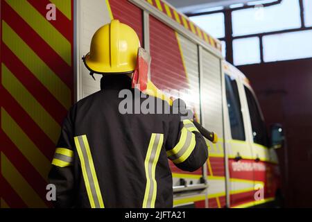 Feuerwehrmann voll ausgestattet mit Helm und Axt im Feuerwehrauto Hintergrund. T Stockfoto