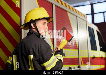 Feuerwehrmann voll ausgestattet mit Helm und Axt im Feuerwehrauto Hintergrund. Stockfoto