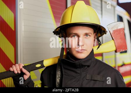 Feuerwehrmann voll ausgestattet mit Helm und Axt im Feuerwehrauto Hintergrund. Stockfoto