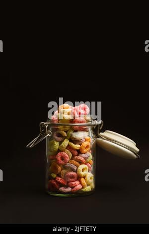 Fruchtaroma gefärbte Cerealien in einem Kristallglas auf schwarzem Hintergrund mit Kopierraum Stockfoto