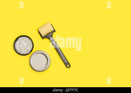 Eine kleine Farbrolle und ein Farbtopf auf gelbem Hintergrund mit Kopierraum Stockfoto