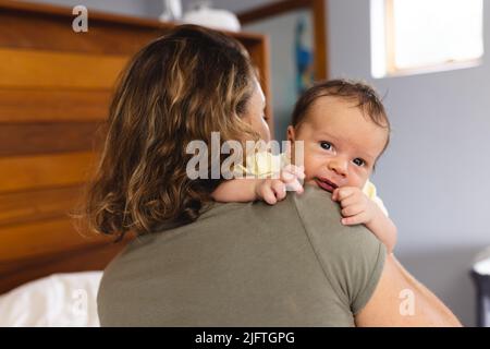 Niedliches neugeborenes Baby, das wegschaut, während es von der kaukasischen Mutter eines mittleren Erwachsenen zu Hause getragen wird. Unverändert, Familie, Liebe, Zweisamkeit, Fürsorge, Unschuld, Motte Stockfoto