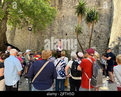 Budva, Montenegro - 06.07.22: Guide führt eine Tour vor Touristen in der Nähe des alten Steingebäudes Stockfoto