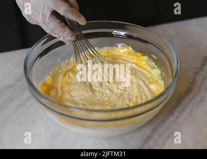 Eine Hand in Gummihandschuh rühren Teig für einen Kuchen Stockfoto