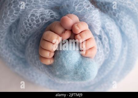 Der kleine Fuß eines Neugeborenen. Nahaufnahme von Zehen, Fersen und Füßen eines Neugeborenen. Gestricktes blaues Herz in die Beine eines Babys Stockfoto