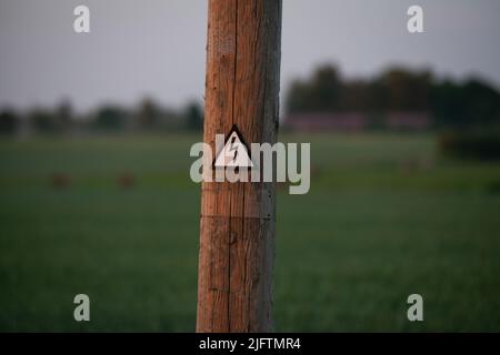 Hochspannungs-Schild auf einem Holzmast. Das Konzept des teuren Stroms. Steigende Energiepreise. Unzugänglicher Strom aufgrund hoher Preise Stockfoto