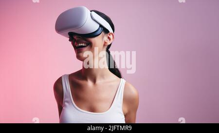 Fröhliche junge Frau in ein lustiges Virtual-Reality-Spiel in einem Studio. Frau lacht fröhlich, während sie ein Virtual Reality-Headset trägt. Weibliche Gamer Exp Stockfoto