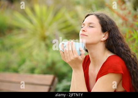 Entspannte Frau, die in einem grünen Park Kaffee riecht Stockfoto