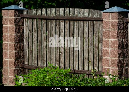 Paneele eines klassischen Holzgefiederten Gartenzauens mit Betonstützen Stockfoto