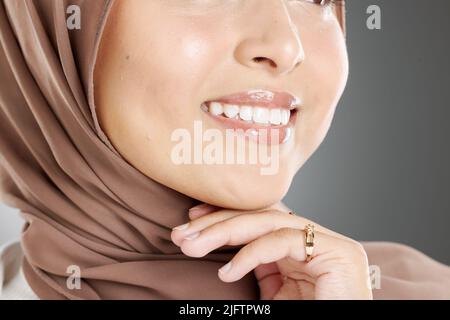 Junge Frau, die einen Hijab oder ein Kopftuch trägt und ihre natürlich aussehenden Veneers nach einer Zahnbehandlung zeigt. Nahaufnahme eines muslimischen Frauengesichts und Stockfoto