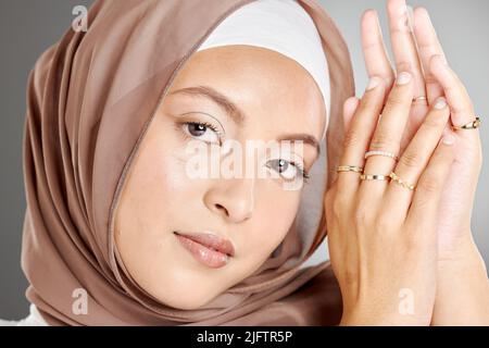 Studioporträt einer schönen muslimischen Frau, die ein braunes Kopftuch trägt und mehrere Ringe an ihren Händen zeigt. Frau trägt Hijab und glühendes Make-up Stockfoto