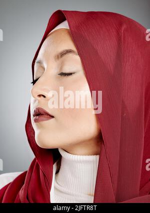 Nahaufnahme einer glühenden schönen muslimischen Frau mit Wimpern-Erweiterungen isoliert vor grauem Hintergrund im Studio. Junge Frau trägt einen roten Hijab oder Stockfoto