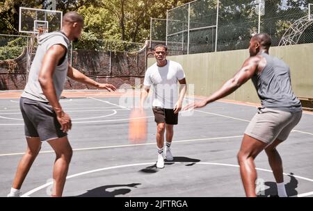 Drei afroamerikanische Männer, die auf einem Platz im Freien Basketball spielen. Der Schwarze und seine sportlichen Freunde sind draußen sportlich. Basketballgruppe Stockfoto