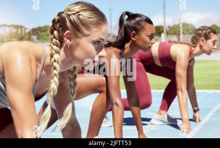 Drei Athletinnen an der Startlinie bei einem Bahnrennen im Stadion. Junge sportliche Frauen in einem Rennen warten und bereit zu laufen. Vielfältig Stockfoto