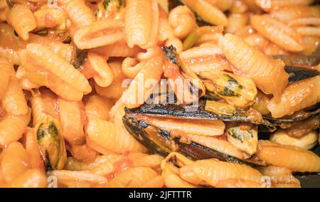 Nahaufnahme eines typisch italienischen Gerichts. Sardische Gnocchi mit schwarzen Muscheln mit Tomaten, Zwiebeln, Knoblauch und Pfeffer. Stockfoto