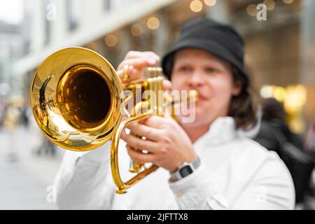 Junger kaukasischer Mann in weißem Hemd und Hut, der draußen Jazz auf Trompete spielt Stockfoto