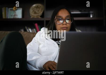 Junge hispanische Frau, die von zu Hause aus mit ihrem Laptop arbeitet Stockfoto