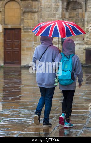 Touristen, die im August an einem regnerischen Tag in Oxford, Oxfordshire, Großbritannien, unter dem Regenschirm von Union Jack bei strömendem Regen Schutz finden Stockfoto