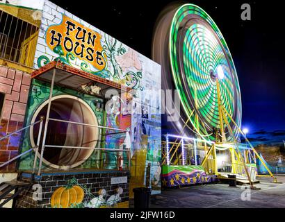 Ein Riesenrad dreht sich neben einem Funhouse auf der Broward County Fair im Gulfstream Park in Hallandale Beach, Florida. Stockfoto