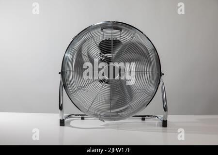 Silberner Metallbodenventilator auf dem weißen Boden zu Hause oder im Geschäft mit grauer Wand. Stockfoto