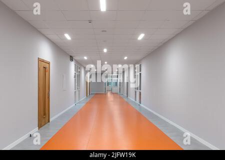 Leerer Schulkorridor. Orangefarbener Boden. Stockfoto