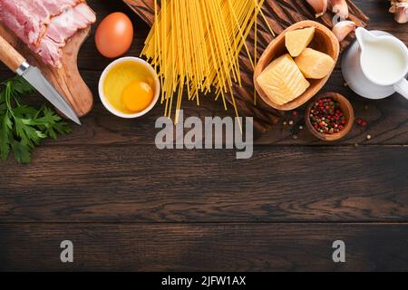 Zutaten für Pasta Carbonara. Traditionelle italienische Pasta Carbonara Zutaten Speck, Spaghetti, Parmesan und Eigelb, Knoblauch. Alter Tisch aus dunklem Holz Stockfoto