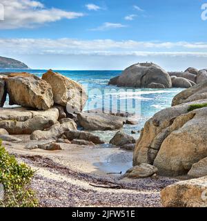 Landschaft von schönen großen Felsbrocken im Meer mit einem blau bewölkten Himmel. Felsen oder Granitstrukturen, die unter der Sonne in der Nähe von ruhigen, schäumenden Wellen an einem scheinen Stockfoto