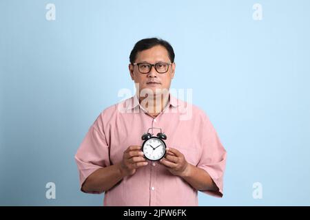 Der Erwachsene asiatische Mann mit rosa Hemd auf dem blauen Hintergrund stehen. Stockfoto