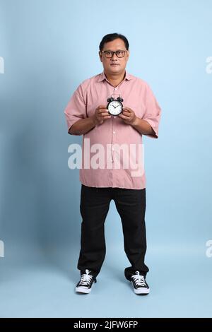 Der Erwachsene asiatische Mann mit rosa Hemd auf dem blauen Hintergrund stehen. Stockfoto