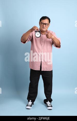 Der Erwachsene asiatische Mann mit rosa Hemd auf dem blauen Hintergrund stehen. Stockfoto