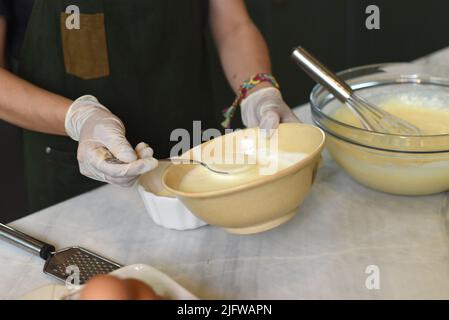 Hände in Gummihandschuhen, die Eigelb in einer Schüssel rühren Stockfoto