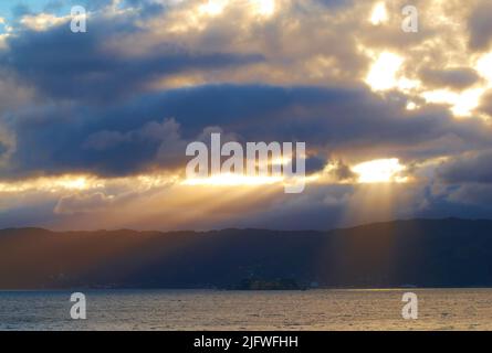 Sonnenlicht bricht durch dunklen, wolkigen Copyspace über einem ruhigen Ozean. Sonnenlicht, das am frühen Morgen durch dicke Wolken scheint. Lichtstrahlen, die ein Stockfoto