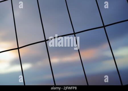 Eiserner Zaun in vertikalen, horizontalen Linien vor einem unscharfen Himmel Hintergrund. Drahtgitter in rechteckigen Formen für Sicherheits- oder Sicherheitskonzept. Die Textur von Stockfoto