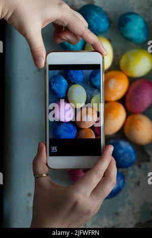 Frau macht Fotos von ostereiern auf dem Smartphone, Draufsicht Stockfoto