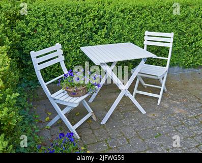 Zwei Stühle und Tisch im Innenhof in einem abgeschiedenen und privaten Garten zu Hause. Hölzerne Terrassenmöbel und Sitzbereich für Kaffee und Lesen in einem Hinterhof Stockfoto