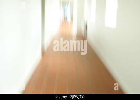 Ein verschwommener gefliester Flur mit weißen Wänden und Sonne, die durch die offenen Fenster scheint. Ein leeres Krankenhaus, eine Klinik oder ein Schulkorridor Stockfoto