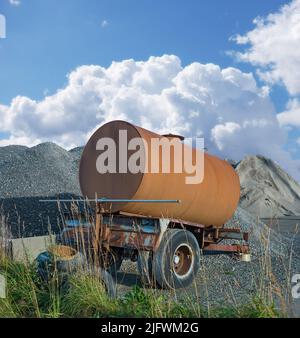 Alter Tanker verfällt auf der Baustelle. Verrostete Wasserbehälter in der Nähe eines Haufens aus Beton und Zement. Verlassene alte rostige Wasser Anhänger Tank in der Nähe Stockfoto