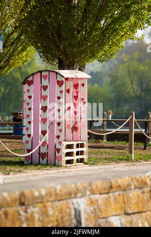 Strandkorb mit roten Herzen. Konstruktion aus Europaletten und Holz in rosa Farbe. Sitzplätze am See. Stockfoto