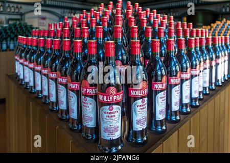 Flaschen von Noilly Prat Rouge mit roten Verschlüssen sind im Laden der Hauptgeschäftsstelle in Marseillan, Hérault, Frankreich, zu einer Pyramide gestapelt. Der Wermut enthält 29 Kräuter und Gewürze aus der ganzen Welt, darunter Zimt, Chinarinde, Nelken und Kakaobohnen, und passt zu herzhaften Gerichten wie Salami oder zu Schokoladendesserts. Noilly Prat Rouge wurde 1956 für Marilyn Monroes Manhattan-Cocktail kreiert – das Getränk, das Billy Wilders Komödie "Einige mögen es heiß" weltberühmt machte. Stockfoto