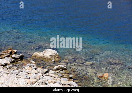 Luftaufnahme zum Meeresstrand mit Steinen auf dem Grund. Sommerküste an sonnigen Tagen, transparentes türkisfarbenes Wasser als Hintergrund Stockfoto