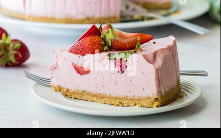 Eine Scheibe Erdbeerkäsekuchen mit dem Rest des Kuchens dahinter. Stockfoto