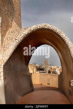 Kamine und Lüftungstürme, La Pedrera (Casa Milà, Antoni Gaudi, 1905-10), Barcelona, Katalonien, Spanien mit La Sagrada Familia hinten Stockfoto