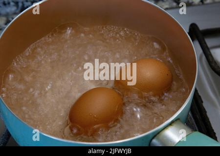 Hühnereier, die in Wasser in einem hellblauen Topf auf dem Herd kochten. Stockfoto
