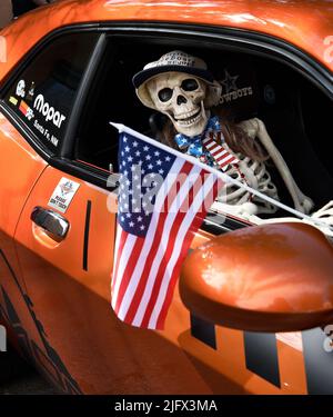 Ein neuheitliches Kunststoff-Skelett hält eine amerikanische Flagge in einem Dodge Challenger aus dem Jahr 2011, der auf einer Automobilausstellung am 4. Juli in Santa Fe, New Mexico, ausgestellt wird. Stockfoto