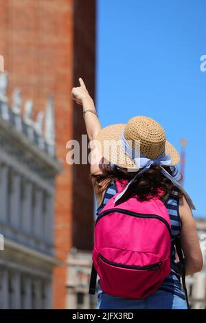 Frau mit Strohhut während der Besichtigungstour in Venedig, die mit ihrer Hand auf den Glockenturm des heiligen Markus zeigt Stockfoto