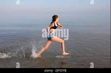 Das sportliche junge Mädchen läuft während des täglichen Trainings schnell auf dem Wasser am Meer Stockfoto