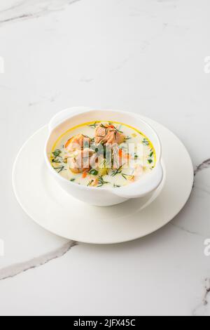 Norwegische Fischsuppe mit rotem Lachs, Gemüse, Kräutern und Rahm, Suppenschüssel auf weißem Marmorboden Stockfoto