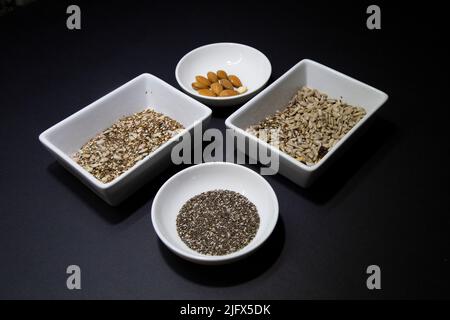 Dunkler Hintergrund mit weißen Schalen enthalten gesunde Samen für eine vegane Ernährung Stockfoto