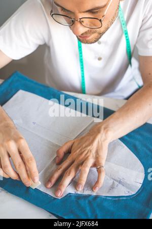 Ein autodidaktischer Seemann in weißem T-Shirt und Brille arbeitet mit Stoff, Muster und Kreide. Ein männlicher DIY-Designer überträgt eine Vorlage auf Stoff. Hobby Stockfoto