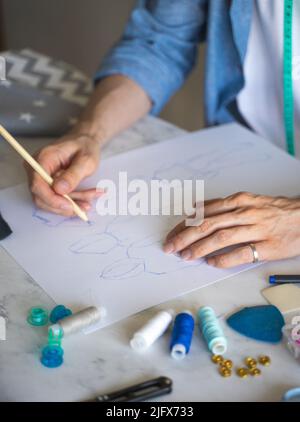 Die Hände des autodidaktischen Schneiders sind auf seiner Skizze. Hand mit Bleistift. Ein DIY Designer zeichnet eine Skizze für ein neues Kostümprojekt. Nahaufnahme, selektiver Fokus Stockfoto